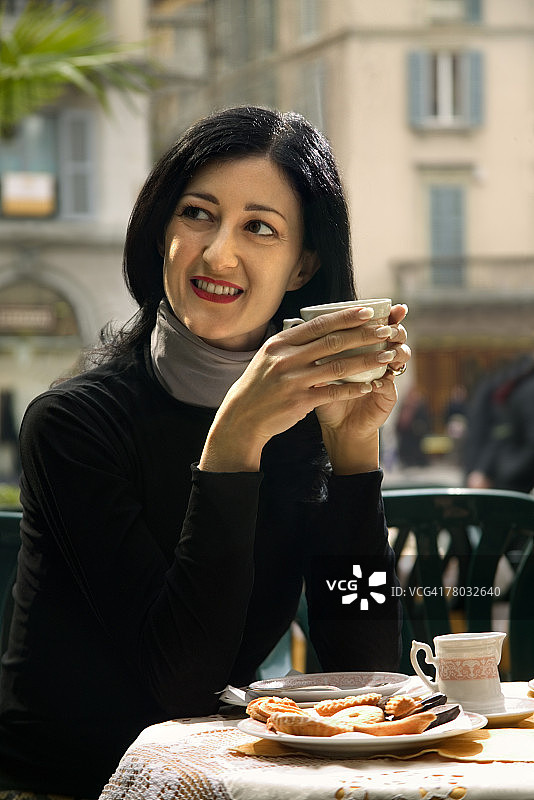 一位女士在咖啡馆里喝茶，面带微笑地看向右边图片素材