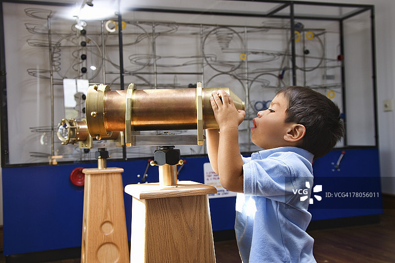 男孩在博物馆里用望远镜观察图片素材