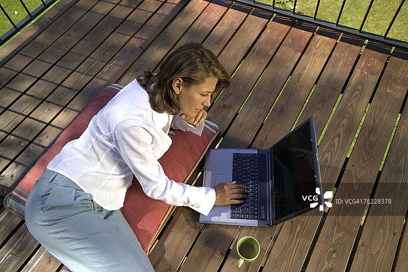 女人躺在门廊上用笔记本电脑工作图片素材
