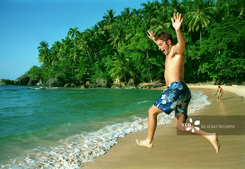 年轻男人在热带海滩跳入海浪图片素材