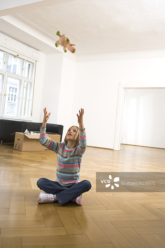 在空旷的公寓里向上抛毛绒玩具的女孩图片素材
