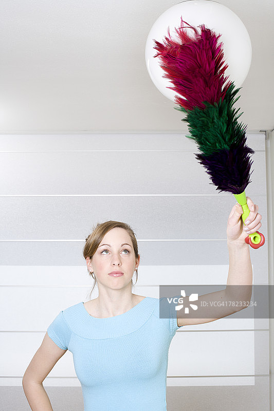 年轻女人用鸡毛掸子掸灯图片素材