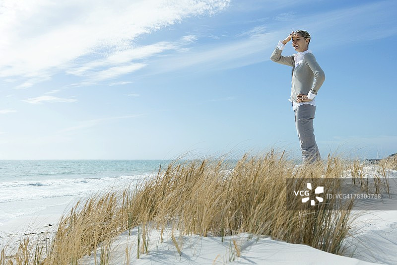 站在沙丘上，遮着眼睛，望向远方微笑的女人，全身照图片素材
