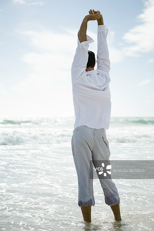 站在海浪中伸展身体的年轻男人（后视图）图片素材