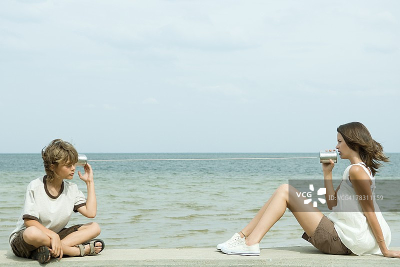 男孩和少女在海边用罐头电话交谈图片素材