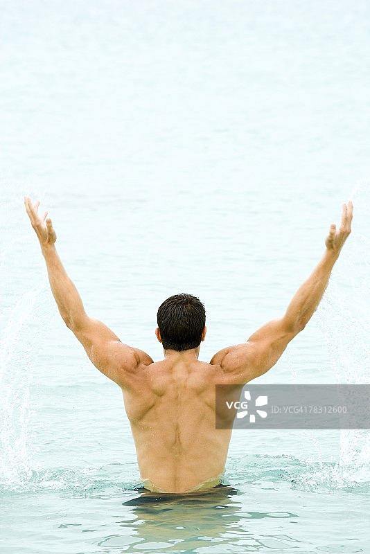 从水中举起双臂的健壮男人（后视图）图片素材