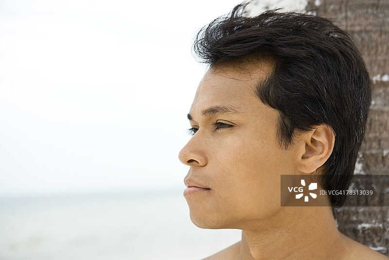 男人倚靠棕榈树头部特写，看向远方图片素材