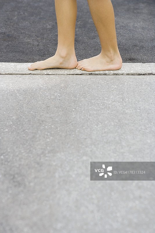 站在水泥边缘的孩子：小腿和赤脚的侧面视角图片素材