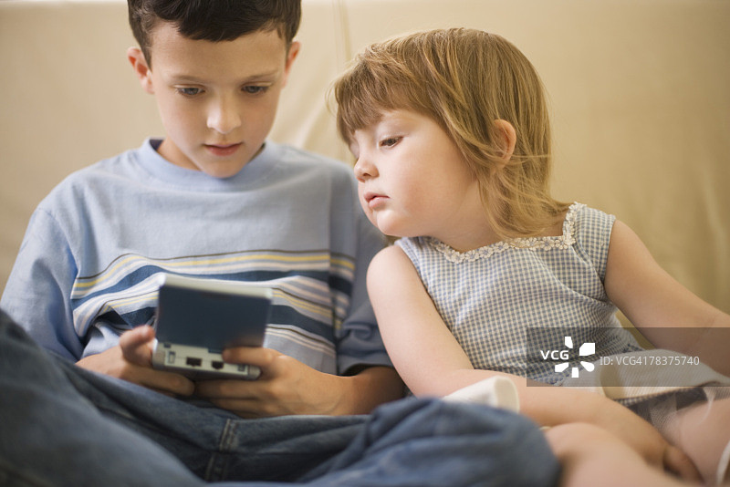 女孩看着她的哥哥玩掌上视频游戏图片素材