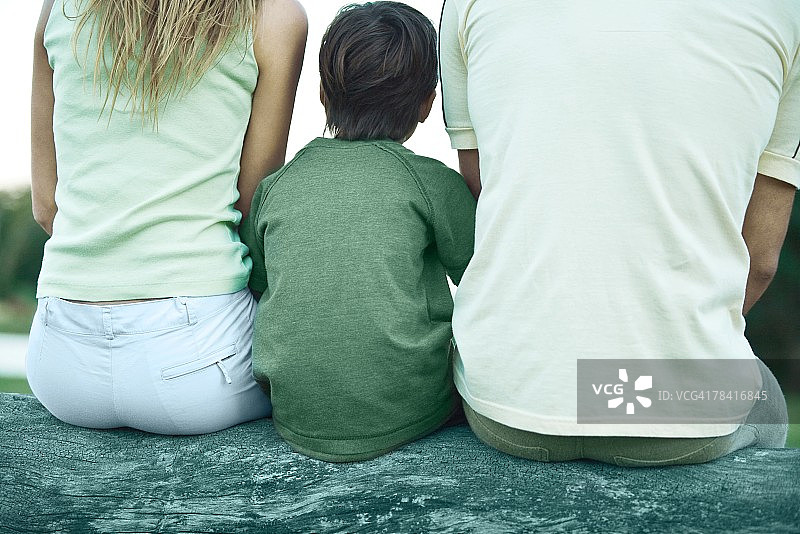 男孩坐在父母之间的圆木上，后视图，局部裁剪图片素材
