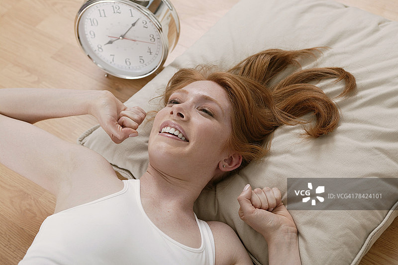 女人在闹钟旁的地板上醒来图片素材