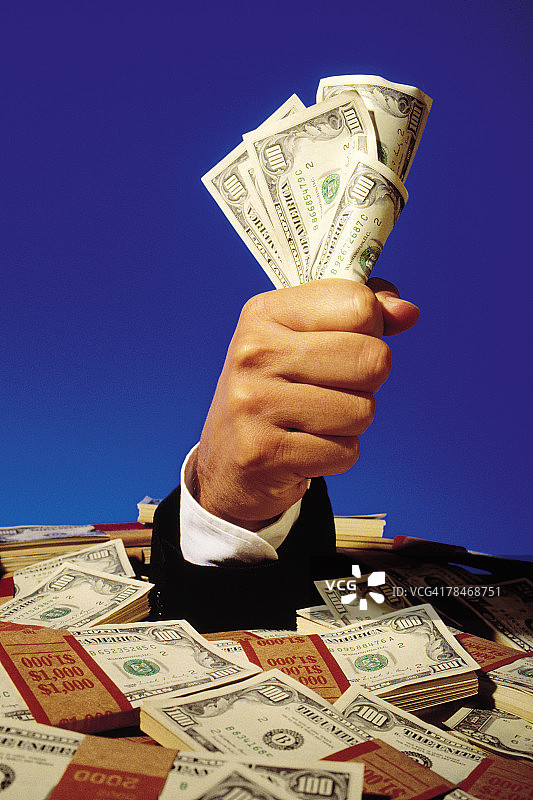 手持从成捆美元钞票中伸出的钱图片素材