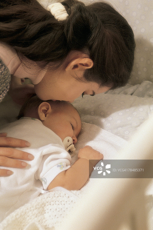 女人亲吻婴儿床里熟睡的宝宝图片素材