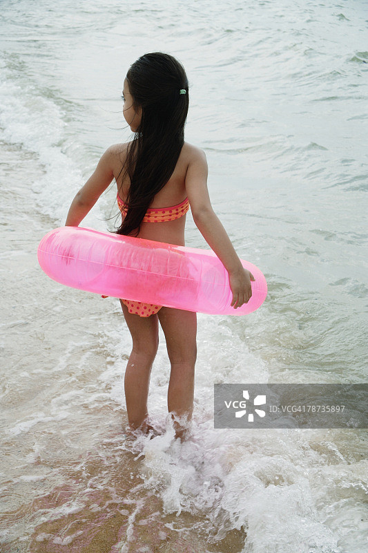 年轻女孩在海滩上穿着比基尼，拿着粉色内胎。图片素材