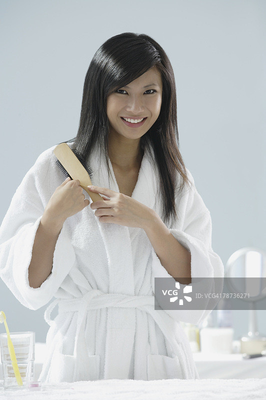 女人穿着浴袍，对着镜头刷头发微笑图片素材