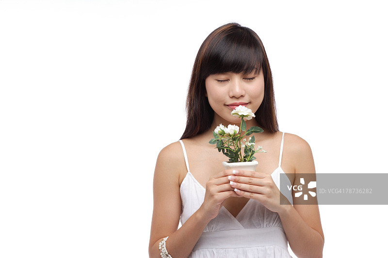 穿着白色连衣裙，拿着小植物，闻着花的年轻女人图片素材
