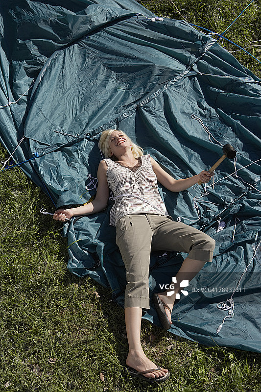 女人手持木槌躺在帐篷上微笑。图片素材
