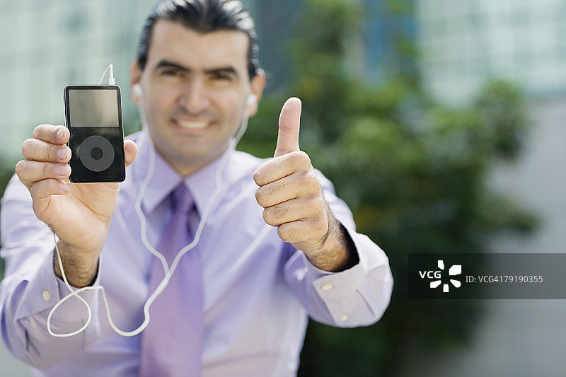 展示MP3播放器并竖起大拇指的商人肖像图片素材