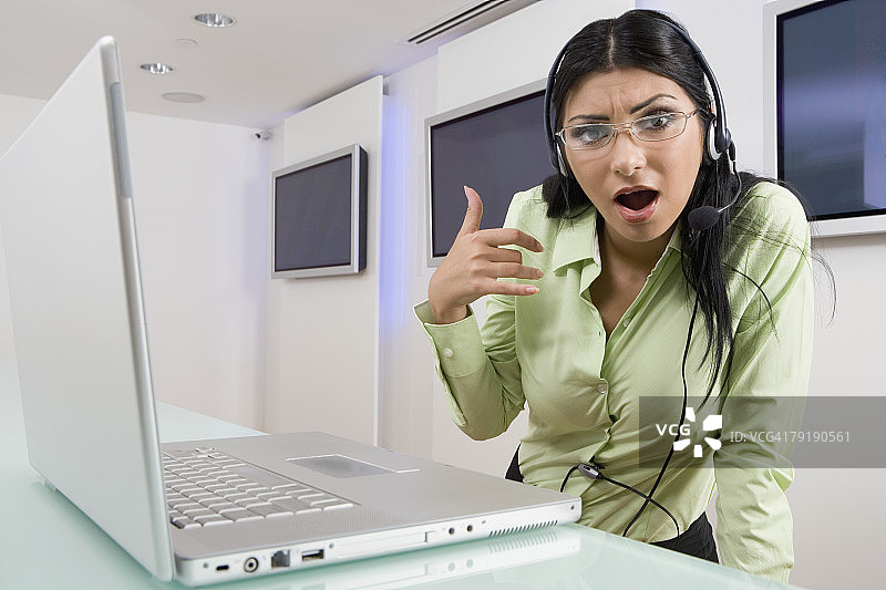 戴着耳机站在笔记本电脑前的年轻女人图片素材