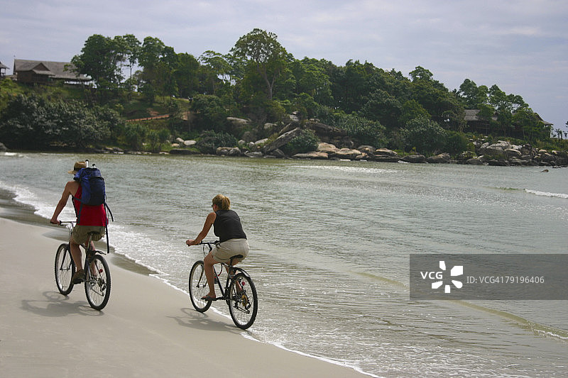 情侣在柬埔寨西哈努克市海滩骑自行车的背影图片素材