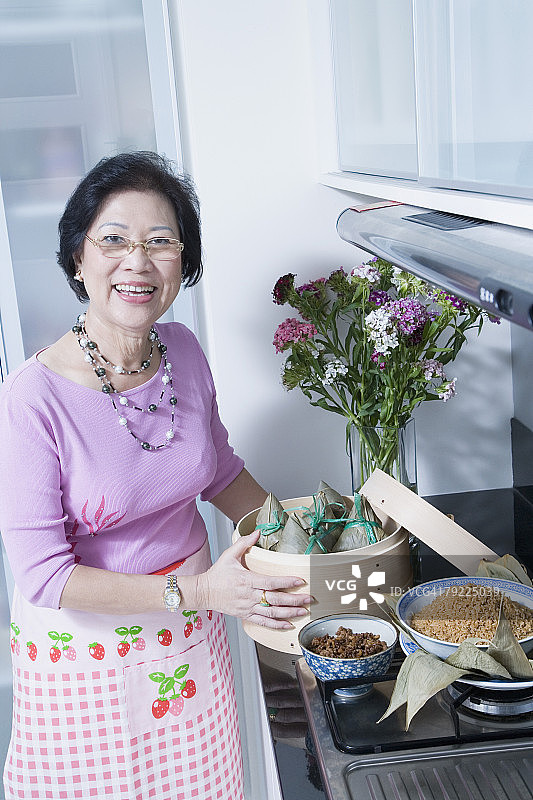 手持竹蒸笼饺子的年长女性肖像图片素材