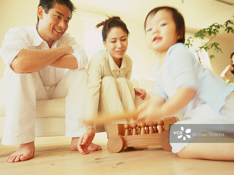 小男孩玩木制玩具，父母在一旁观看图片素材