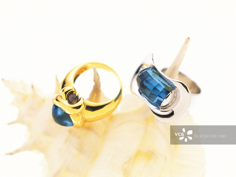 两枚镶嵌蓝宝石的戒指放在海螺壳上，高角度拍摄，白色背景图片素材
