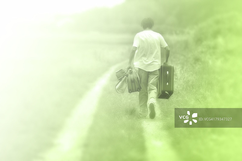 男人提着行李箱在乡间小路上行走（后视图）图片素材
