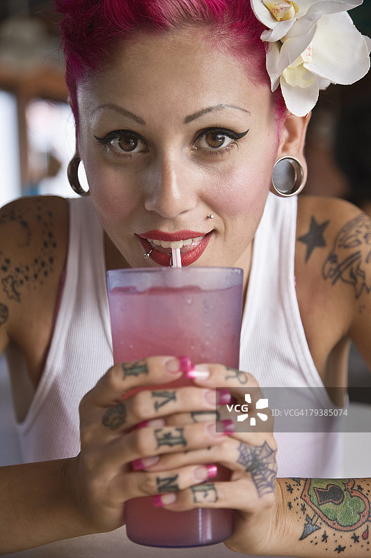 用吸管喝饮料的西班牙裔纹身女人图片素材
