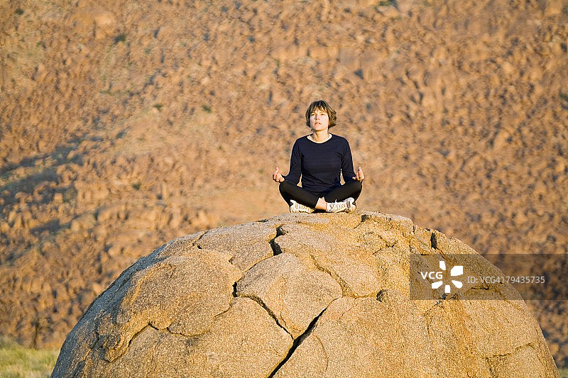 女人在贫瘠的景观岩石上冥想,低角度视图。南非北开普省里赫特斯维尔德国家公园图片素材