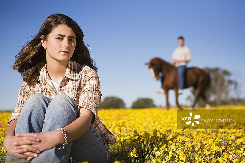 前景中的女人,背景中是在鲜花盛开的纳马夸兰田野里骑马的男人,南非北开普省新瓦特维尔图片素材