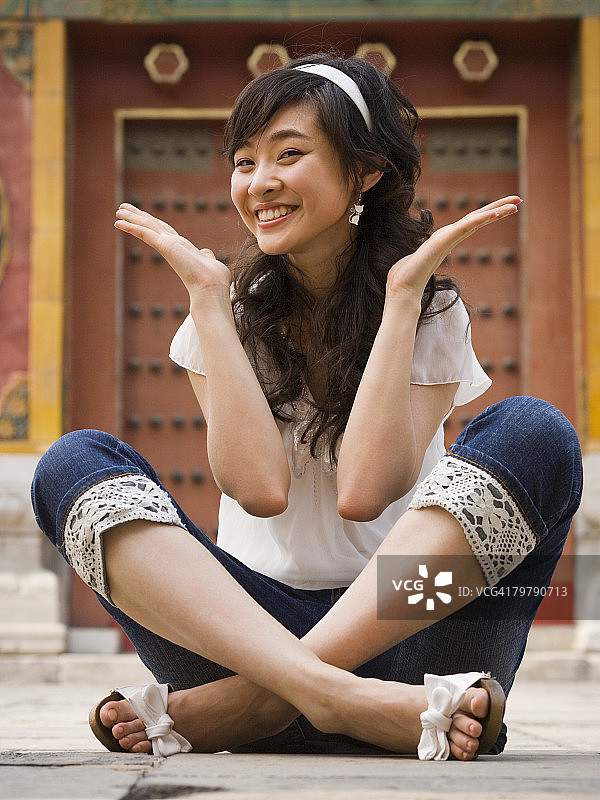 女孩户外盘腿坐着，举手微笑。图片素材