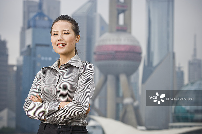女商人在户外微笑，双臂交叉，城市天际线为背景图片素材