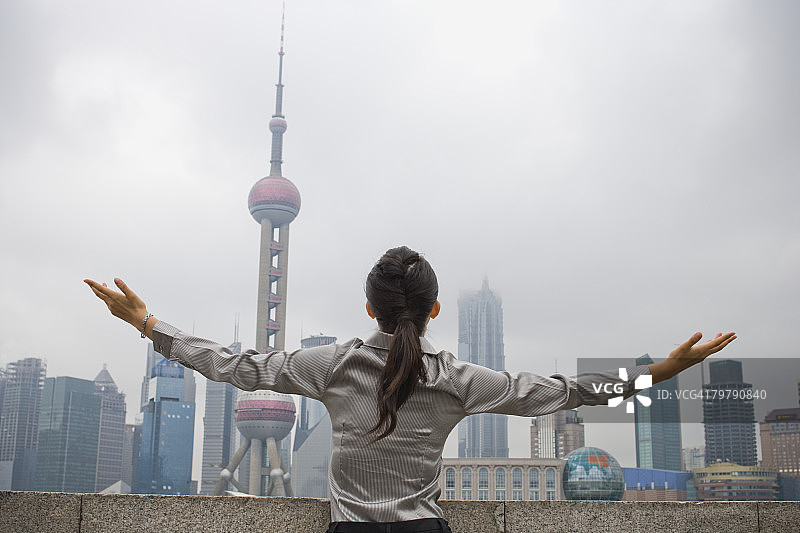 户外张开双臂，以城市天际线为背景的女商人背影图片素材