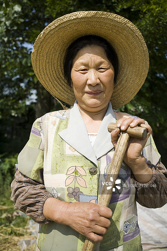 戴着草帽和铲子站在户外微笑的女人图片素材