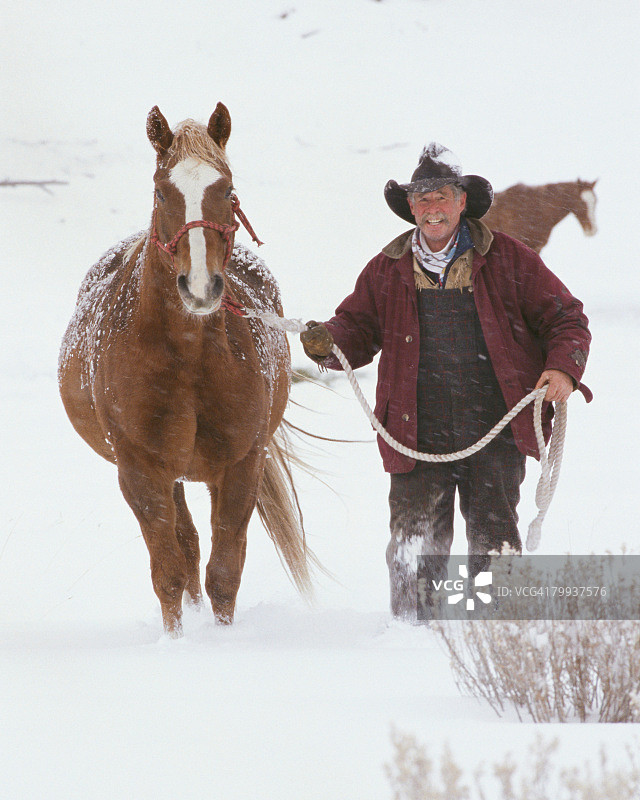 牧场主牵着马穿过雪地图片素材
