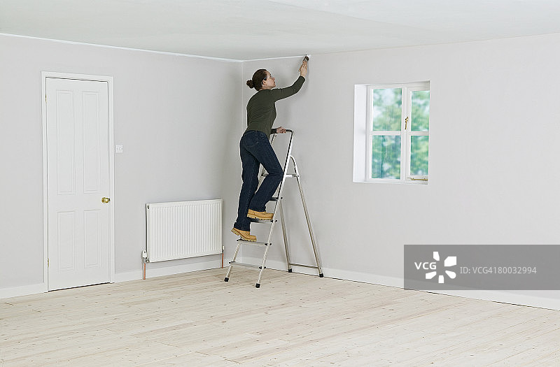 在梯子上粉刷天花板边缘的女人图片素材