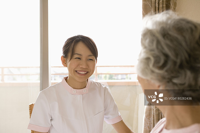 女护士在床上和老年妇女交谈，面带微笑图片素材