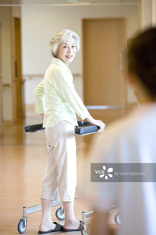 女护士和年长妇女在走廊里使用助行器，聚焦年长妇女图片素材