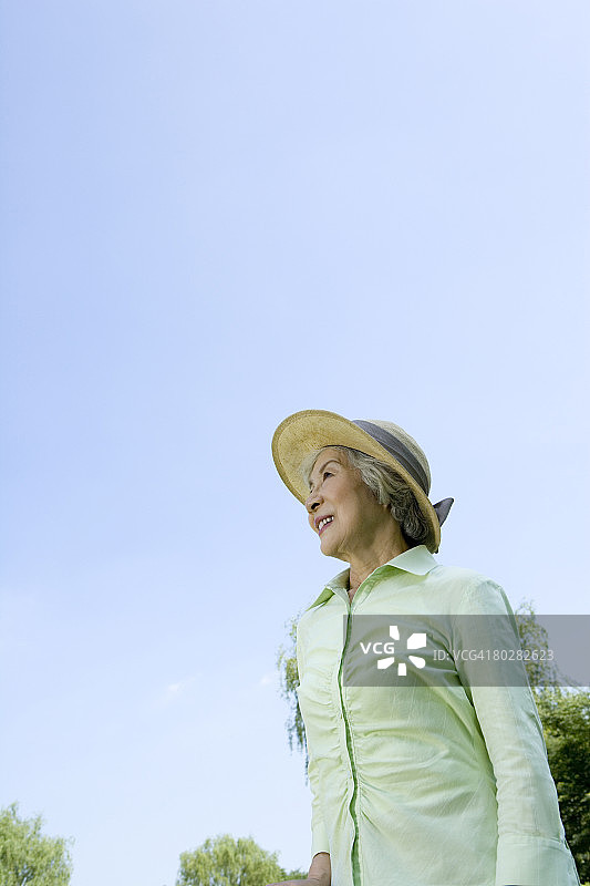 戴帽子的老年妇女微笑抬头看天空，留白图片素材