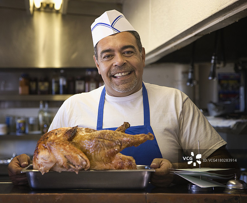 手持烤鸡的西班牙裔男厨师图片素材