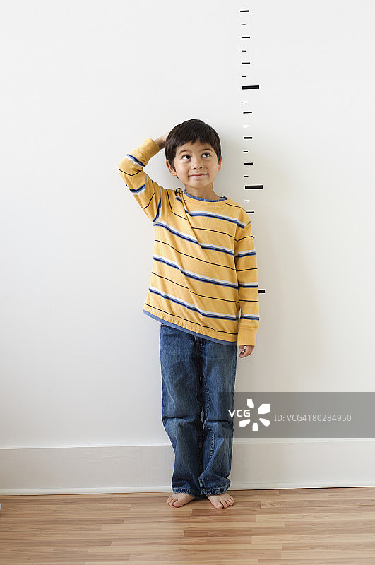 亚洲男孩站在墙上的身高标记旁图片素材
