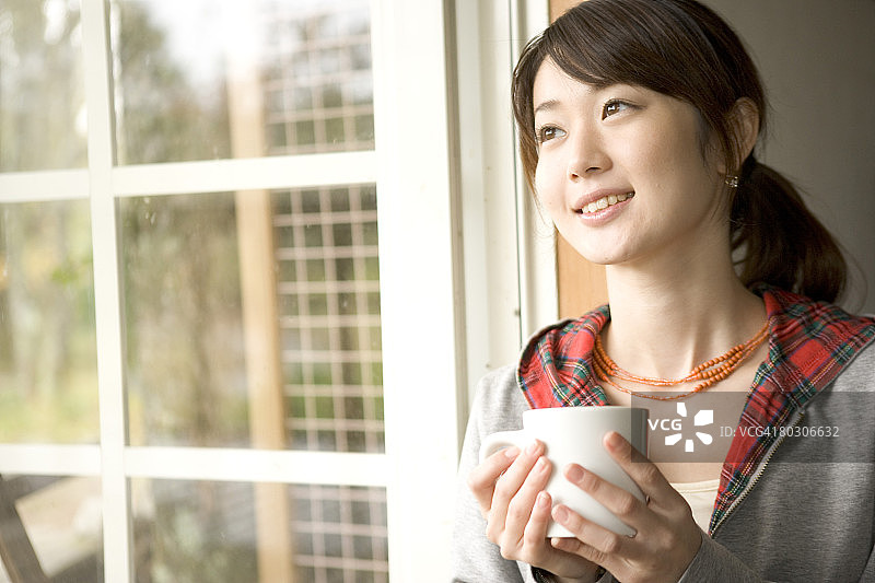 端着杯子望向窗外的女孩图片素材