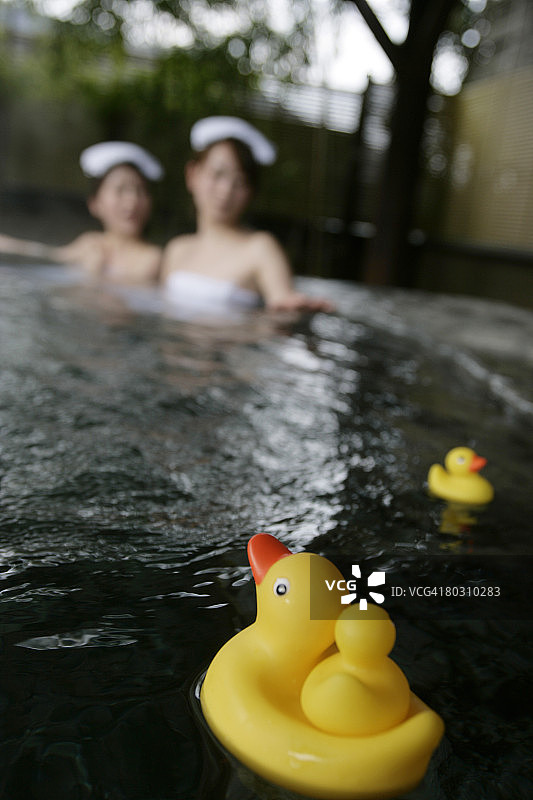 两名女子在热水浴缸中放松，前景中有橡胶鸭图片素材
