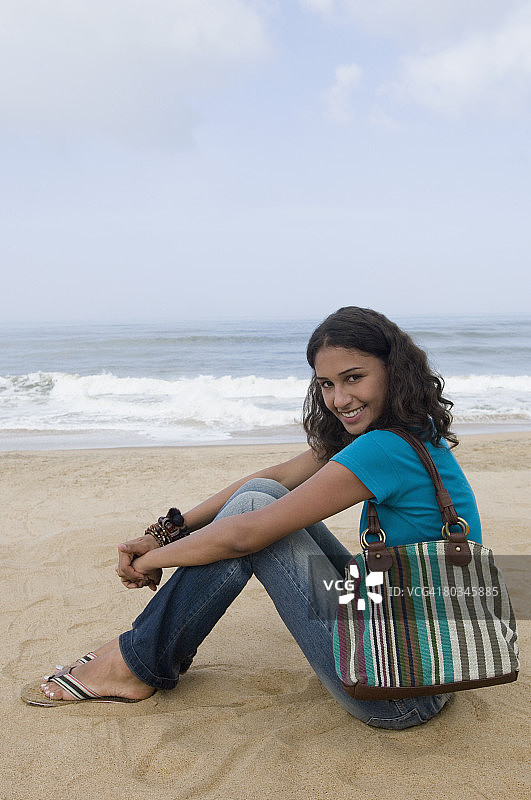 年轻女子坐在沙滩上微笑的肖像图片素材