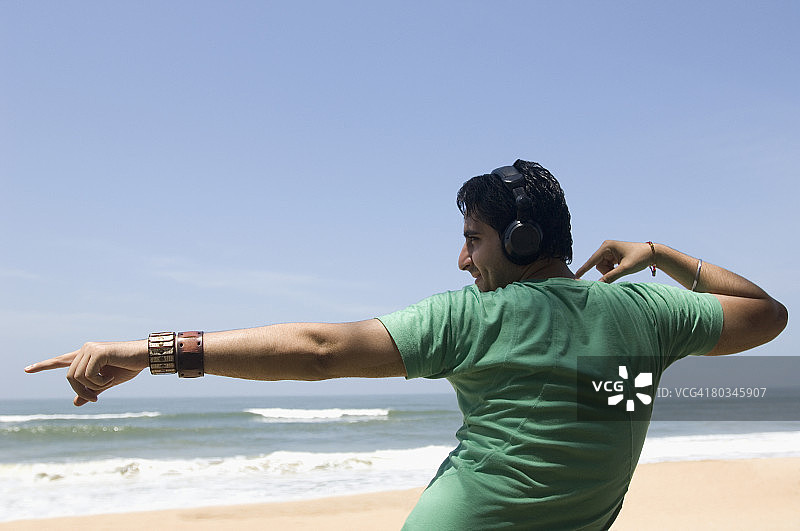 戴着耳机在海滩跳舞的年轻男子的背影图片素材