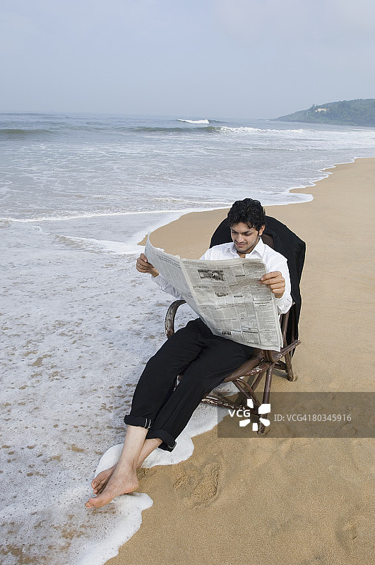 在海滩上阅读报纸的年轻男子图片素材