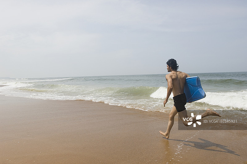 carrying a surfboard and running on the beach图片素材