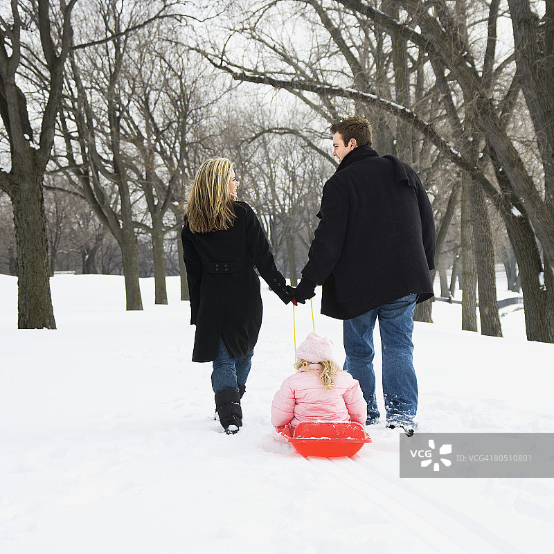 父母拉着雪橇上的女孩图片素材
