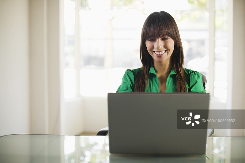 面带微笑的女商人坐在办公桌前使用笔记本电脑图片素材